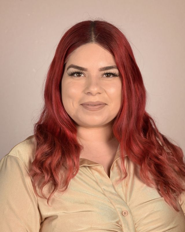 A woman with red hair is wearing a tan shirt and smiling for the camera.