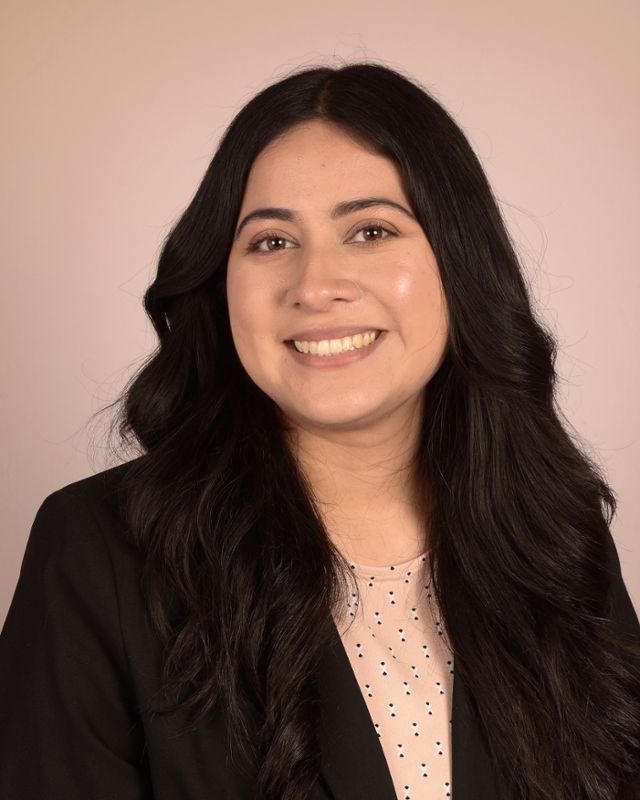 A woman with long black hair is wearing a black jacket and smiling for the camera.