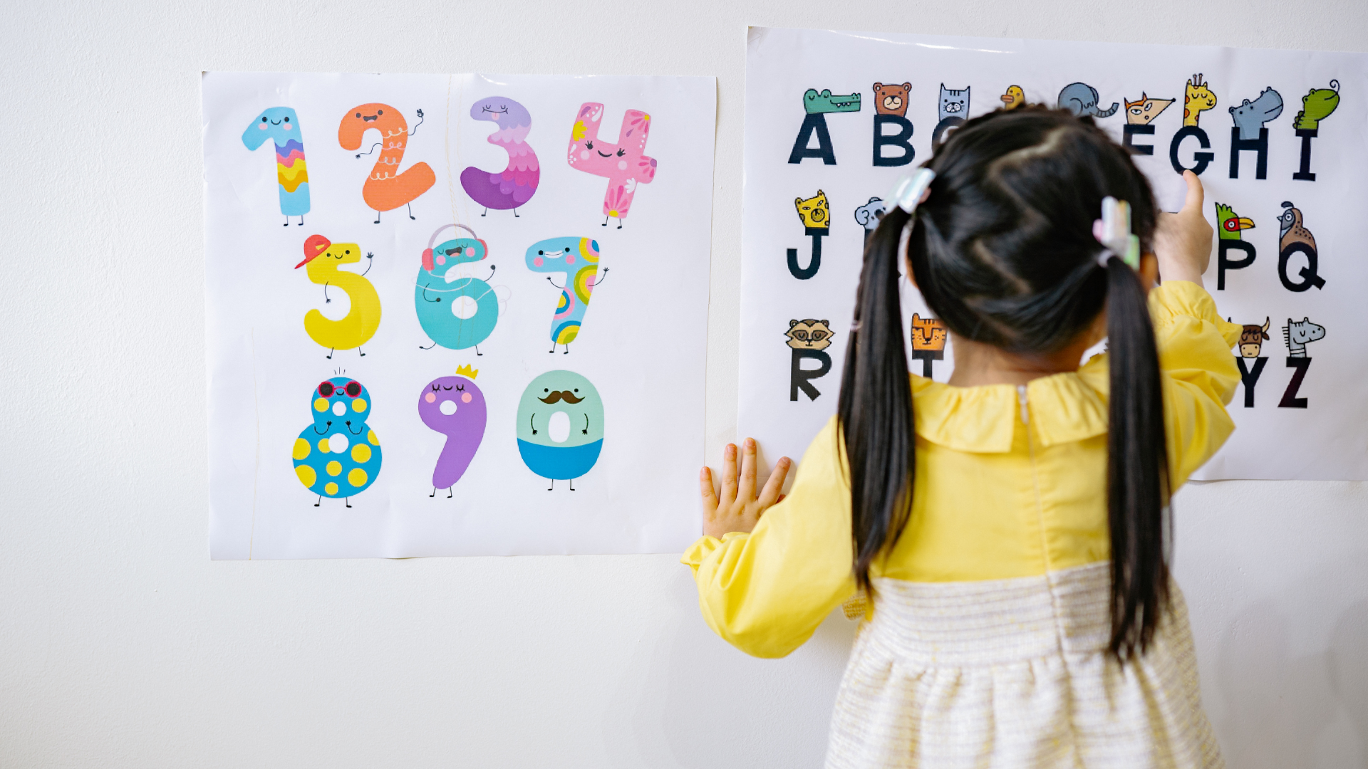 A little girl is standing in front of a wall with numbers and letters on it.