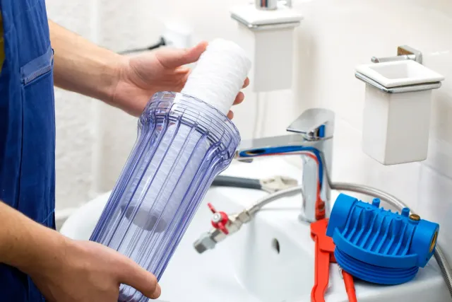A person is holding a water filter in front of a sink.