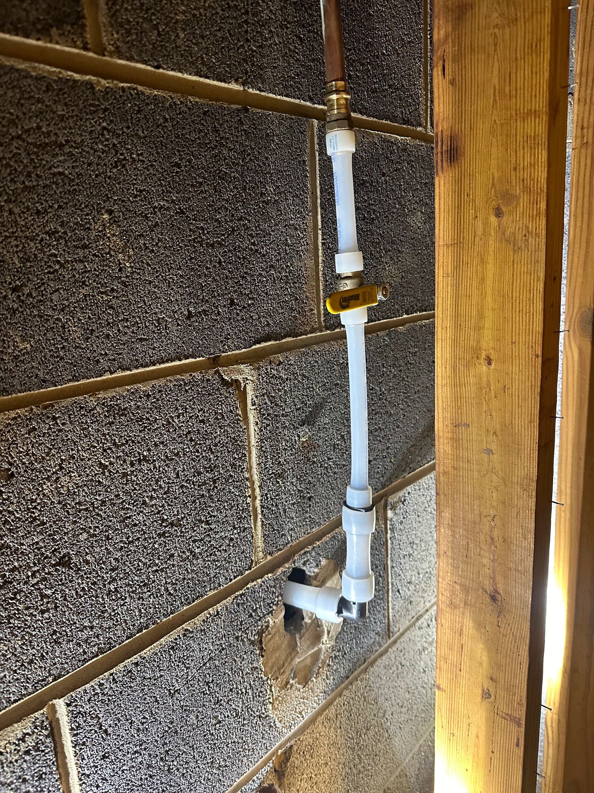 Plumbing pipes attached to a concrete block wall, with a valve.