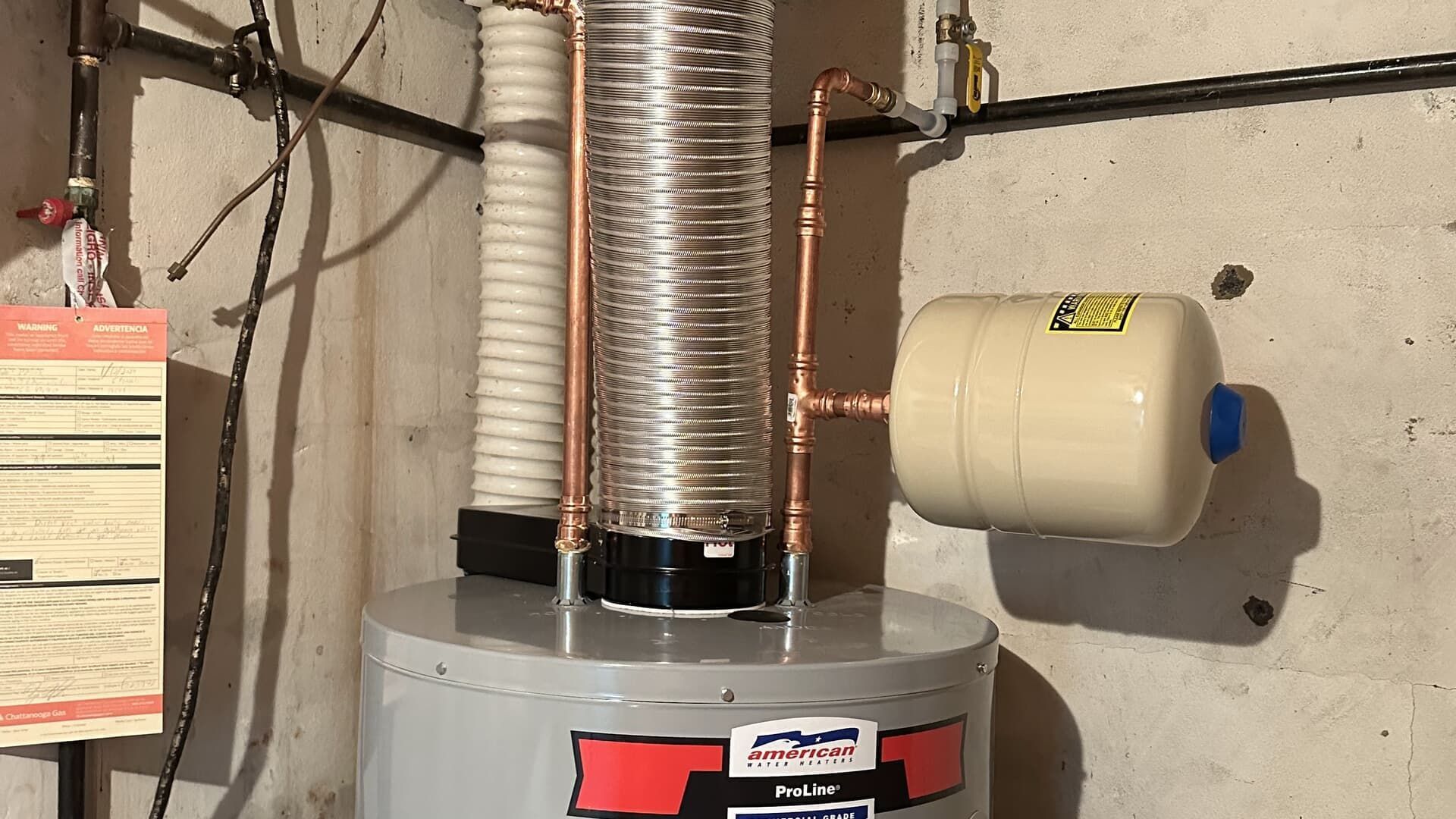 Water heater with copper coil, pipes, expansion tank in basement setting.