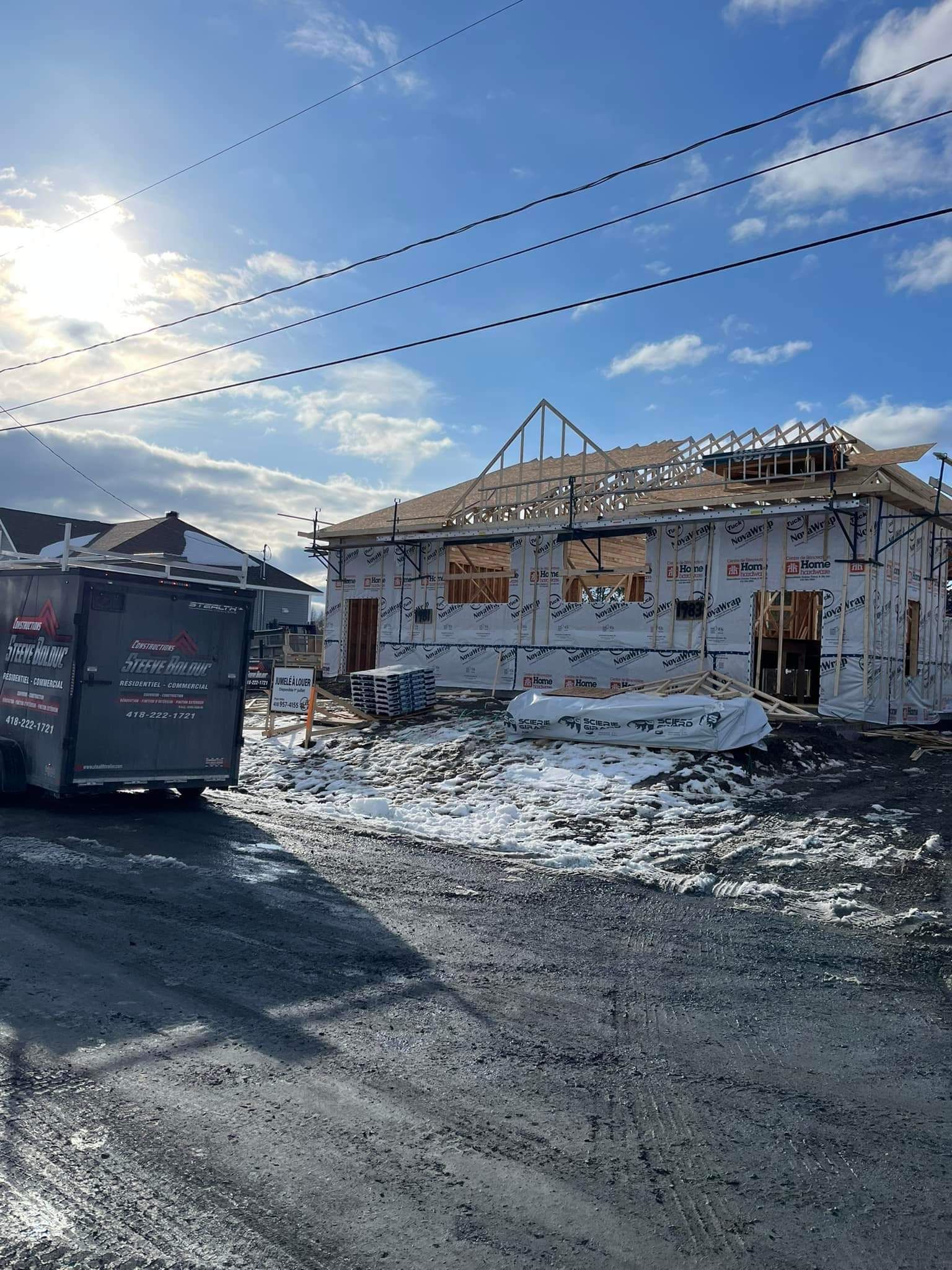 Chantier : maison en construction à ossature bois apparente. Neige et conteneur sur un chemin de gravier.