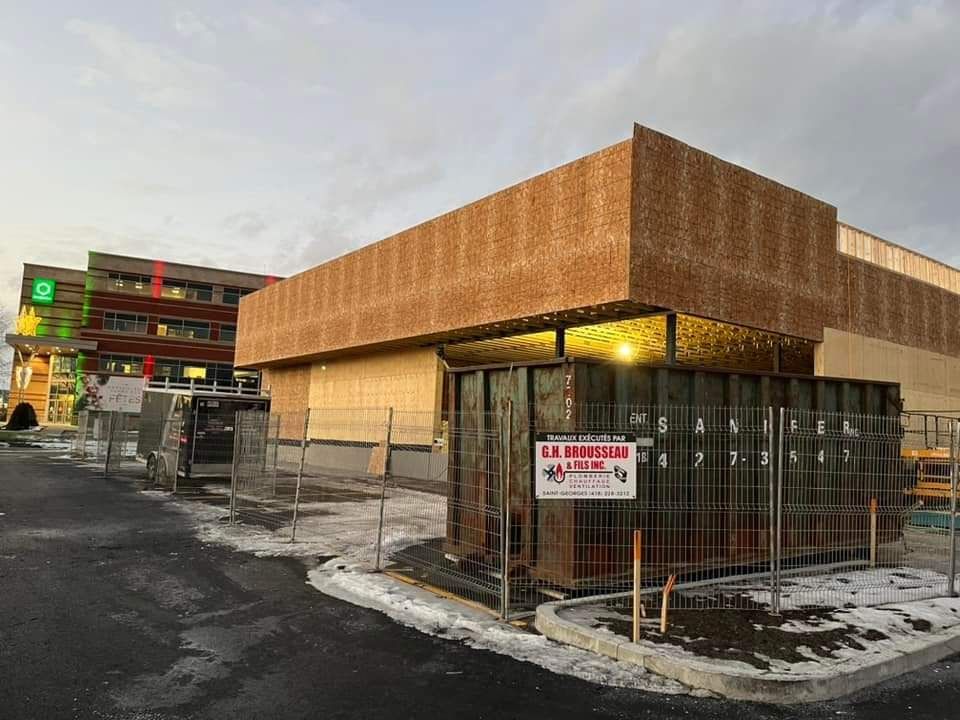 Bâtiment en construction, façade brune, barrières métalliques, ambiance hivernale, enseigne McDonald's visible.