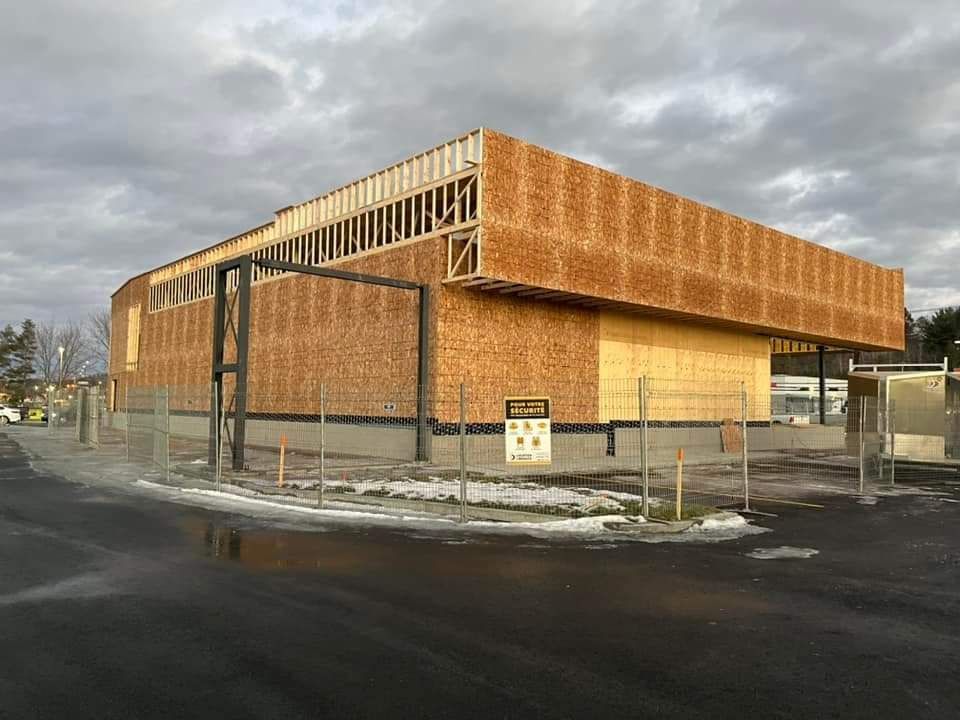 Bâtiment en construction, ossature bois, murs extérieurs, ciel gris.