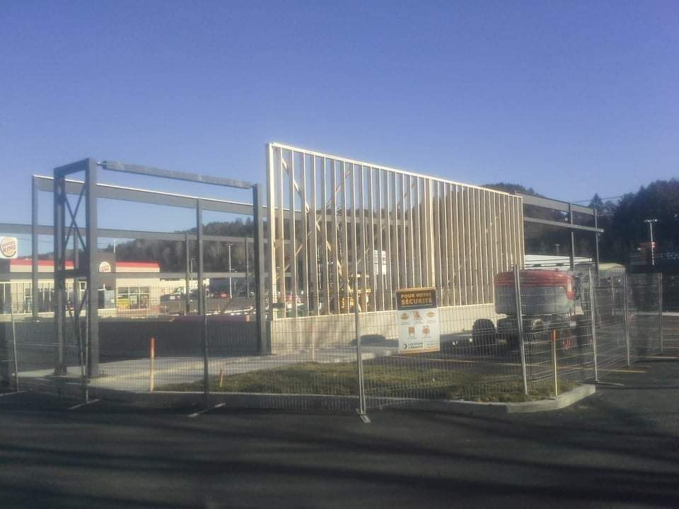 Chantier de construction avec ossature bois et structures de soutien métalliques devant un restaurant Burger King.