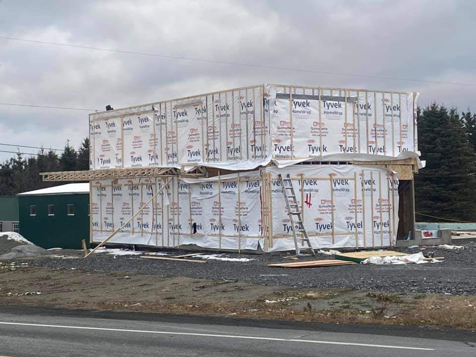 Bâtiment de deux étages en construction, recouvert d'une bâche Tyvek, avec une structure verte à gauche.