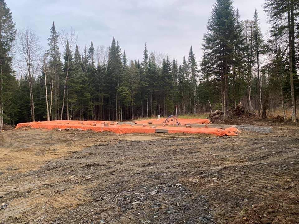 Déblaiement de chantier, filets de sécurité orange et terre. Fond forestier avec ciel nuageux.