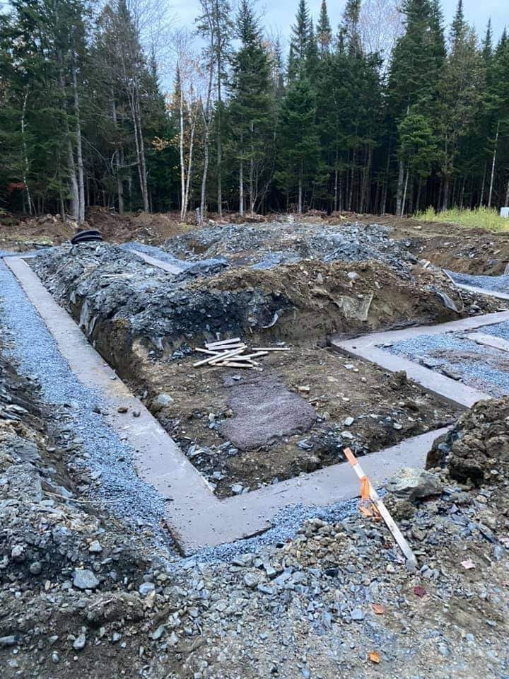 Chantier de construction de fondations avec semelles en béton et terre excavée, entouré de gravier.
