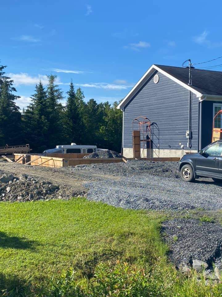Chantier de construction avec fondations, maison bleue, gravier et véhicule par une journée ensoleillée.