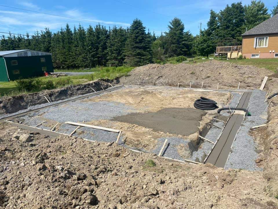 Fondations de piscine en construction, avec gravier gris, béton, tuyaux et terre environnante.