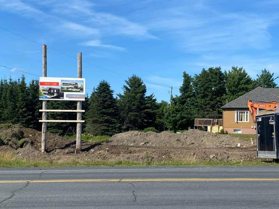 Panneau publicitaire immobilier sur un chantier en bord de route, ciel bleu en arrière-plan.