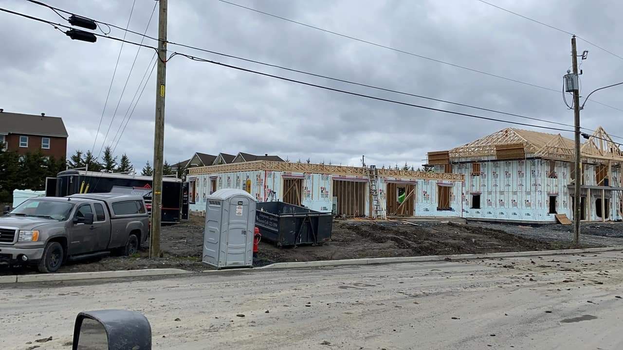 Chantier : charpente en bois, isolation du bâtiment, camion, toilettes portables, ciel couvert.