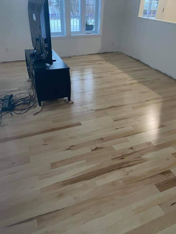 Dans cette pièce, un parquet clair neuf est installé. On aperçoit un meuble TV noir avec un téléviseur.