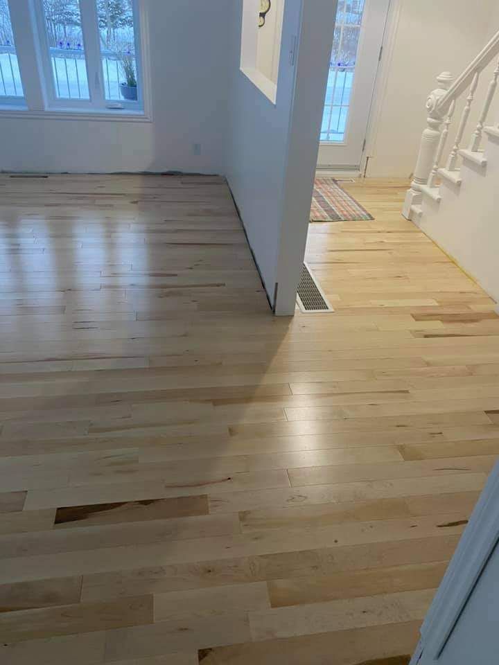 Dans cette maison, le sol est en parquet clair. Un mur blanc sépare le séjour de l'entrée. On aperçoit un escalier.