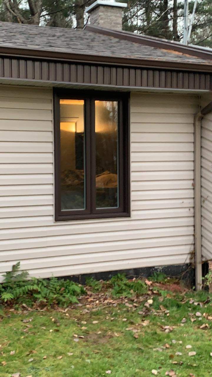 Bardage beige d'un bâtiment avec une fenêtre reflétant une lumière intérieure chaude, situé dans une cour.