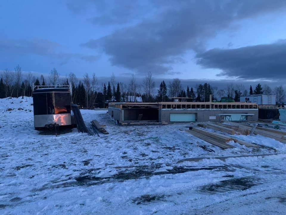 Chantier de construction en hiver ; structure partiellement construite, sol enneigé, ciel nuageux.