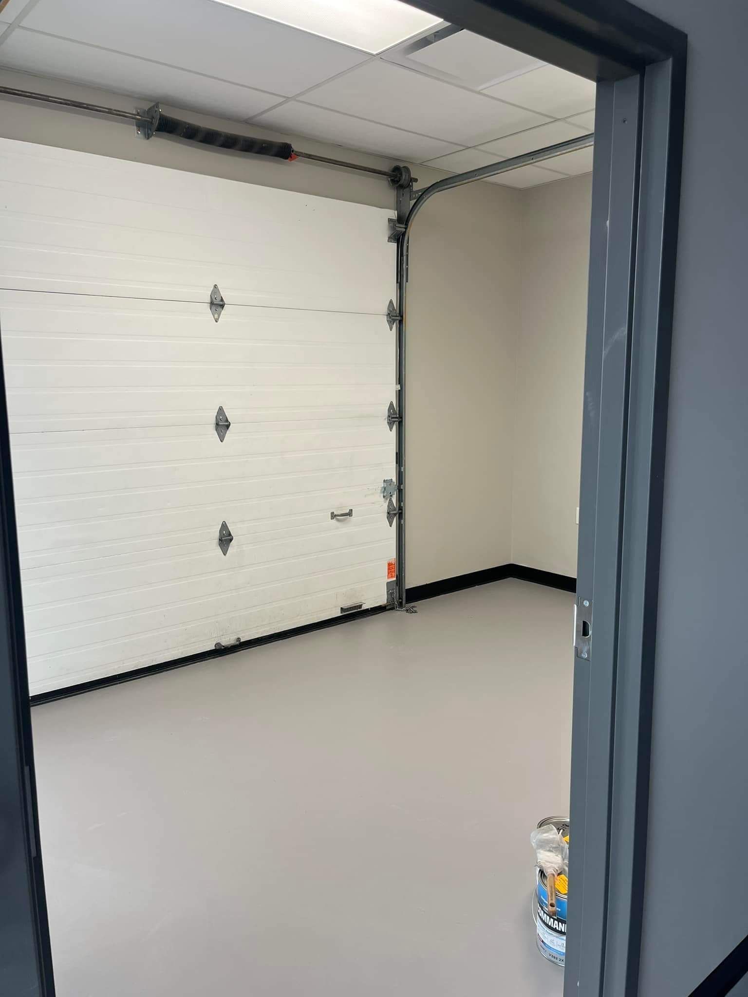 Pièce vide avec une grande porte de garage blanche, un sol gris clair et des murs gris clair.