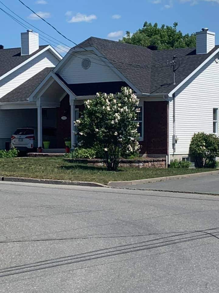 Une maison en briques blanches, au toit sombre, avec une petite voiture garée dans l'allée par une journée ensoleillée.