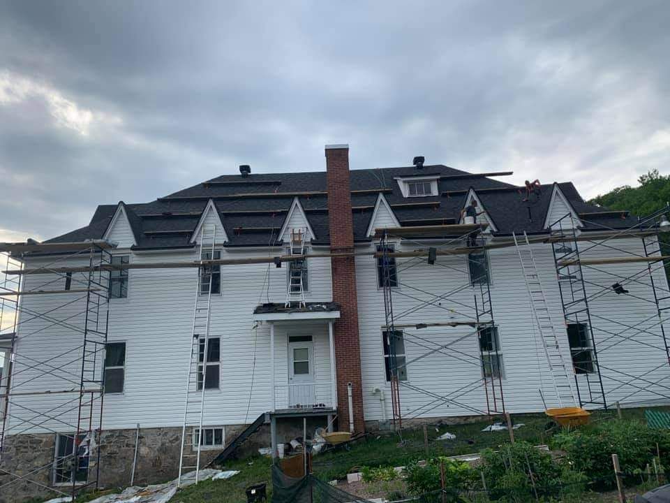 Maison blanche en construction, échafaudages, toiture neuve partiellement installée, cheminée en briques, ciel couvert.