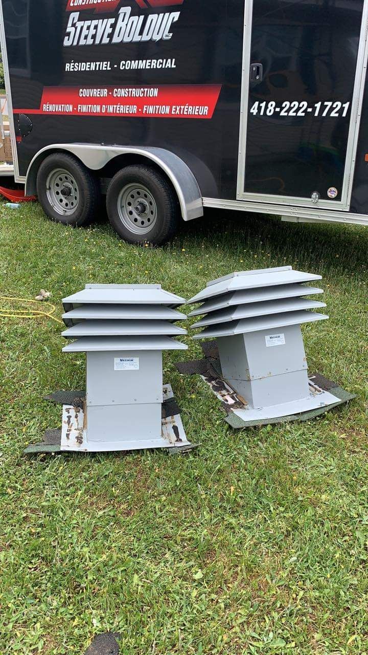 Deux unités de ventilation grises sur le toit, posées sur l'herbe devant une caravane.