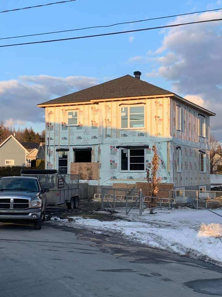 Maison à deux étages en construction, recouverte d'une bâche bleue. Une camionnette est garée dans la rue devant la maison.