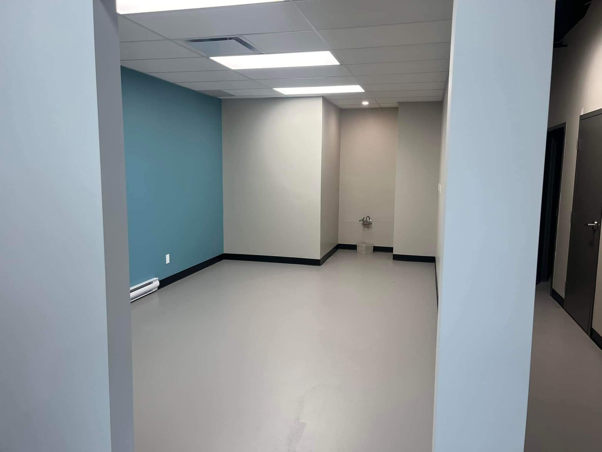 Bureau vide avec murs gris, un mur d'accent bleu clair et un sol gris.