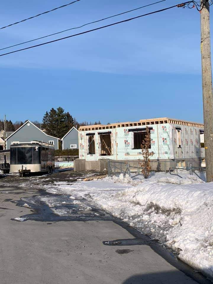 Construction d'une petite maison à ossature apparente et isolation, située dans une rue enneigée.