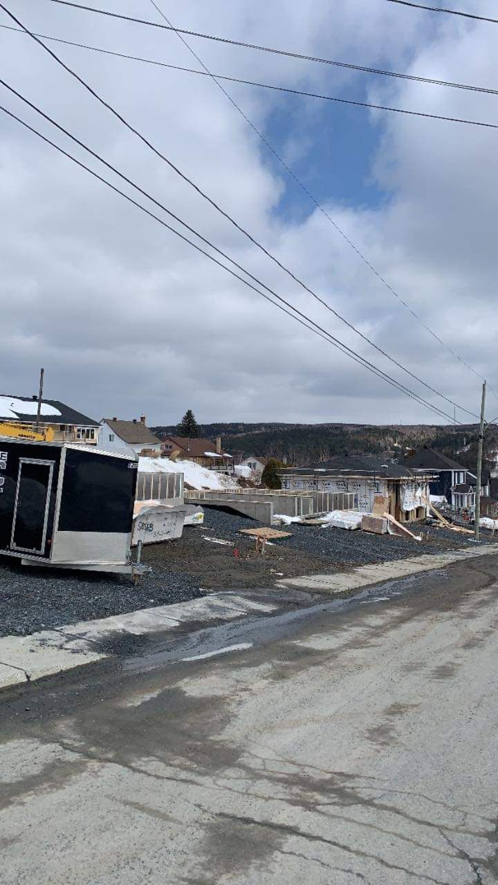 Route de gravier dans un quartier résidentiel, maisons en arrière-plan, lignes électriques au-dessus, ciel nuageux.