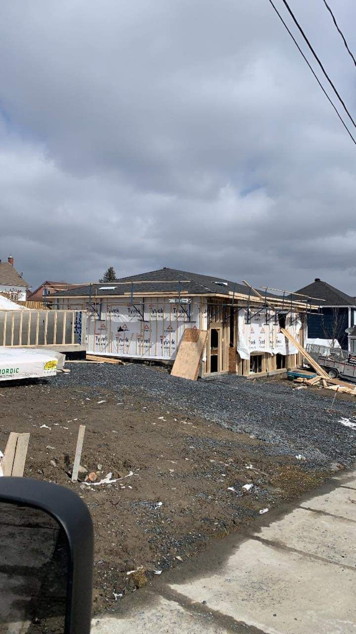 Chantier de construction avec une maison en construction, ciel nuageux au-dessus.
