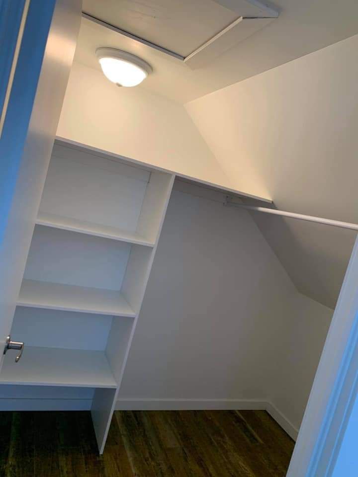 Placard blanc avec étagères et tringle à vêtements, sous un plafond mansardé.