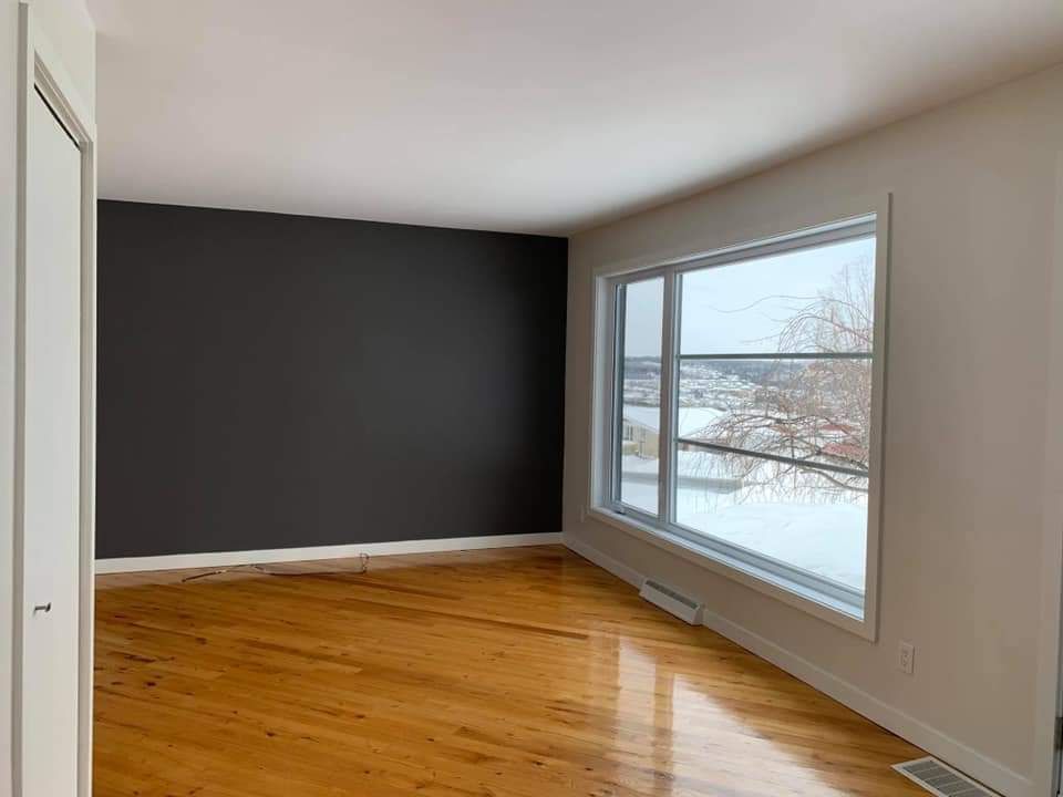 Pièce vide avec parquet, un mur d'accent gris et une grande fenêtre donnant sur un paysage enneigé.