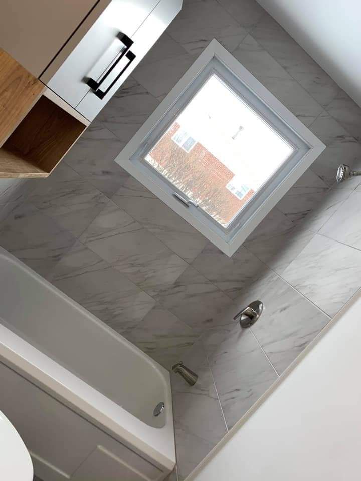 Salle de bains avec carrelage en marbre gris, baignoire, fenêtre et meuble-lavabo blanc et bois.