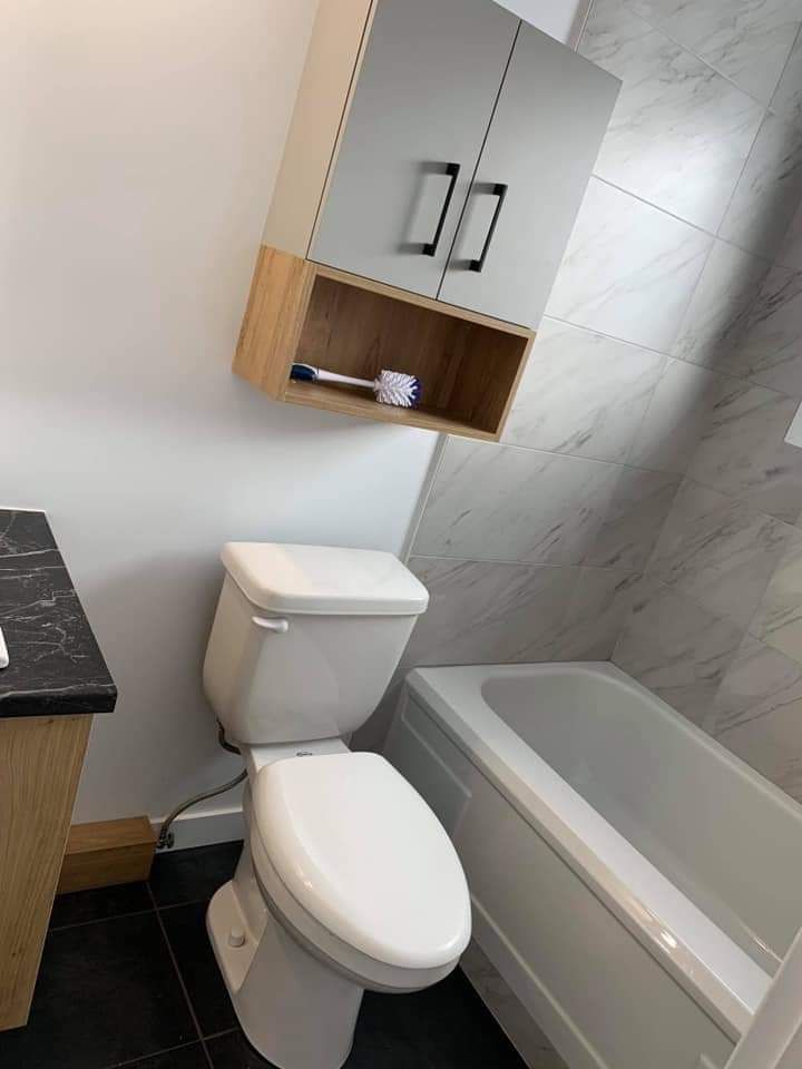 Salle de bains avec toilettes, baignoire et meuble-lavabo. Robinetterie blanche, meuble-lavabo gris et bois.