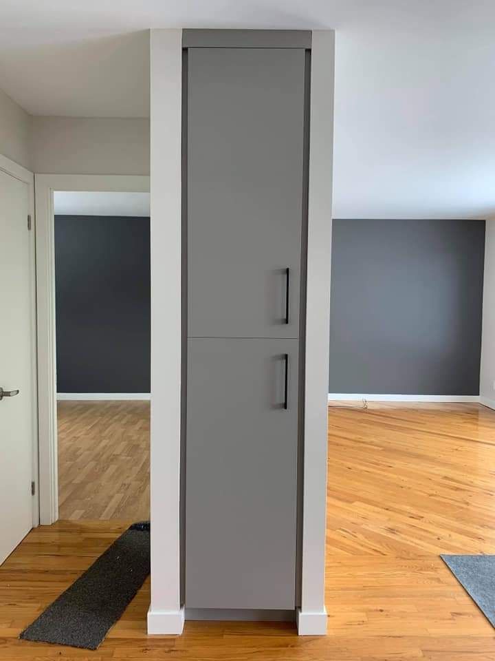 Armoire grise encastrée dans un mur, entre deux pièces aux sols en bois et aux murs gris foncé.