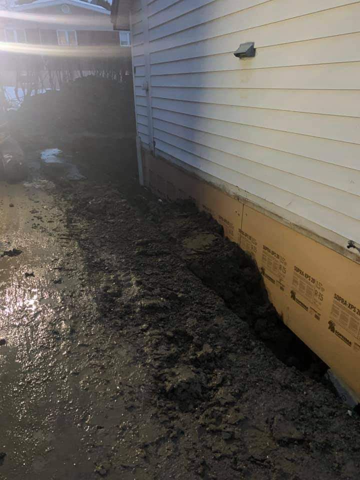 Chemin boueux à côté d'une maison blanche. Du sable brun et humide recouvre le sol.