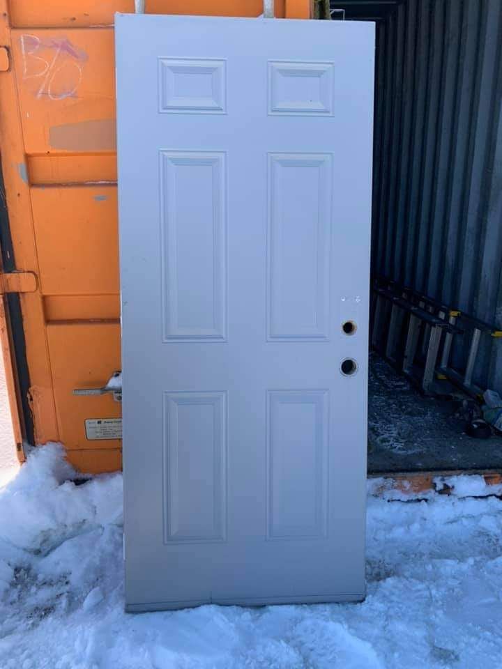 Une porte blanche à six panneaux se dresse dans la neige à côté d'une structure orange.