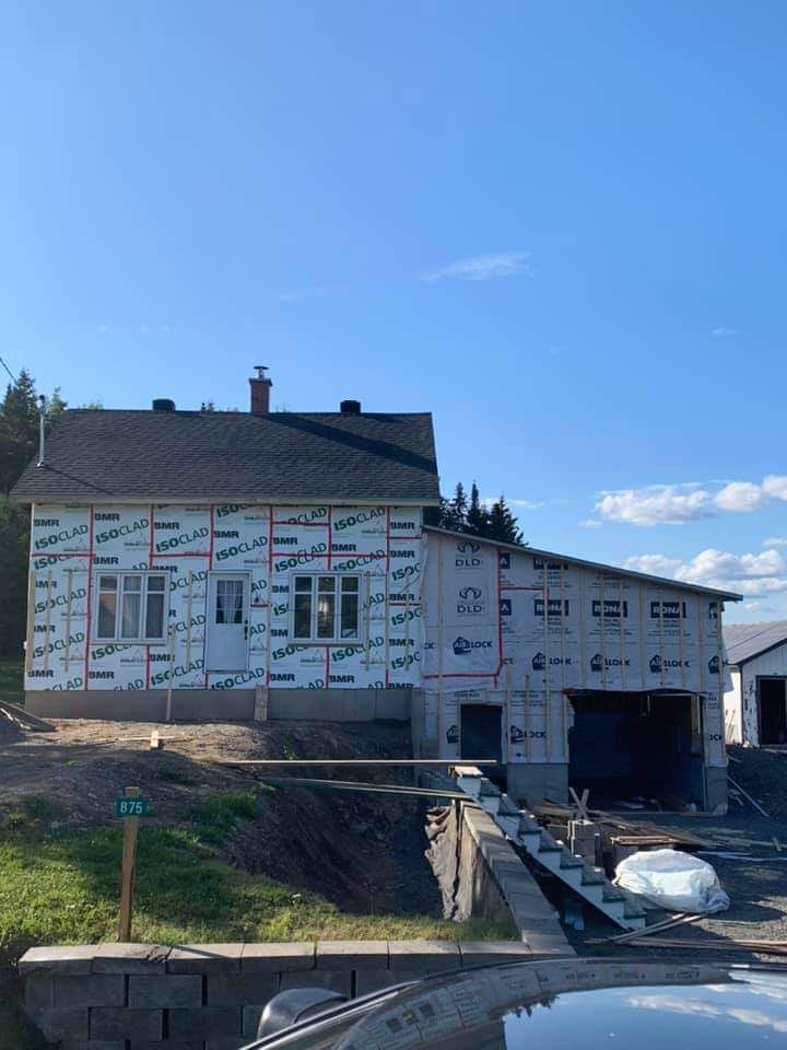 Maison en construction avec garage, recouverte d'une bâche de protection, sur fond de ciel bleu.
