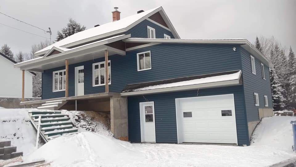 Maison bleue avec porte de garage blanche dans un décor enneigé. Un escalier mène au porche.