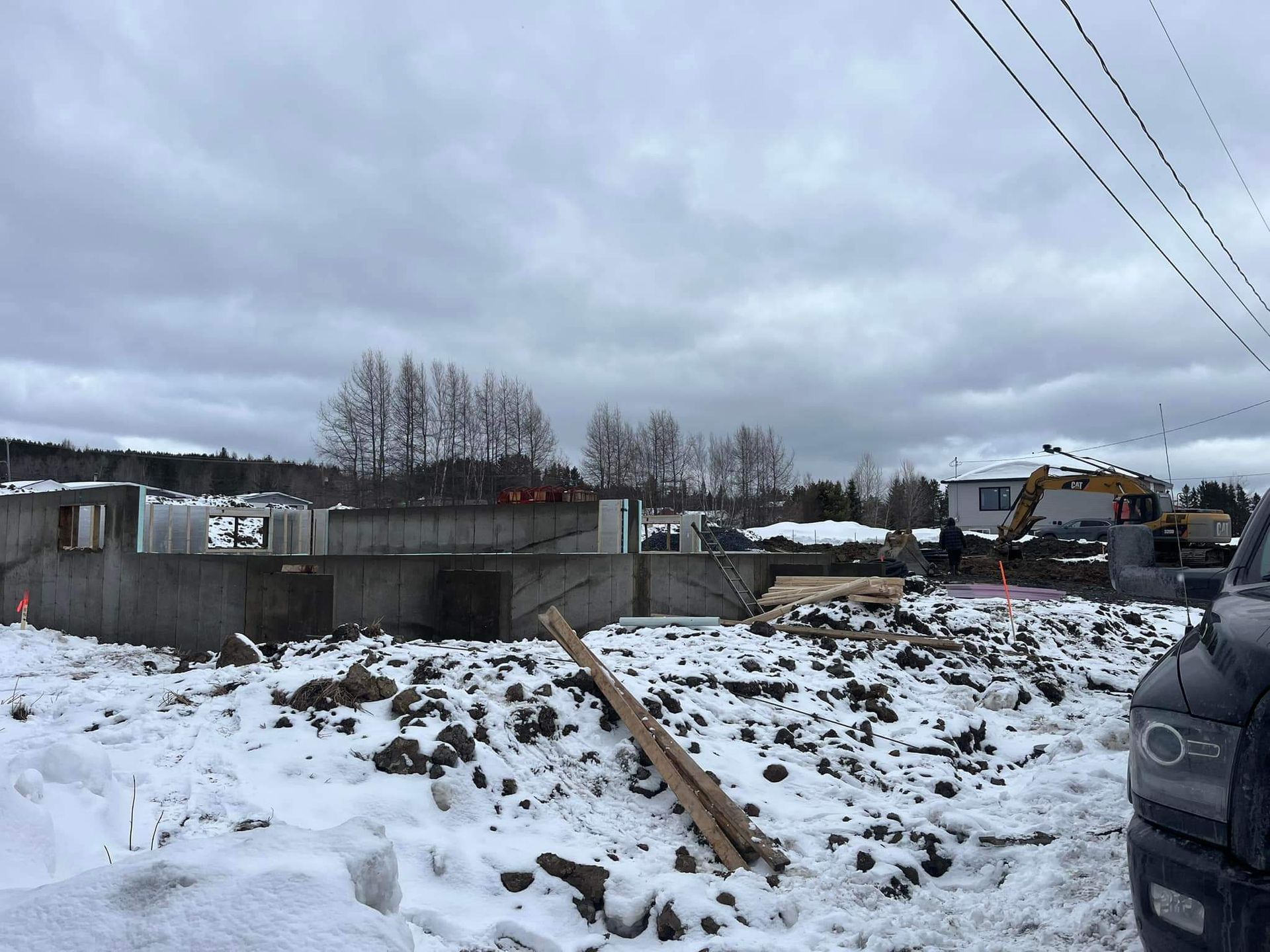 Chantier de construction avec fondations en béton et sol enneigé sous un ciel nuageux.