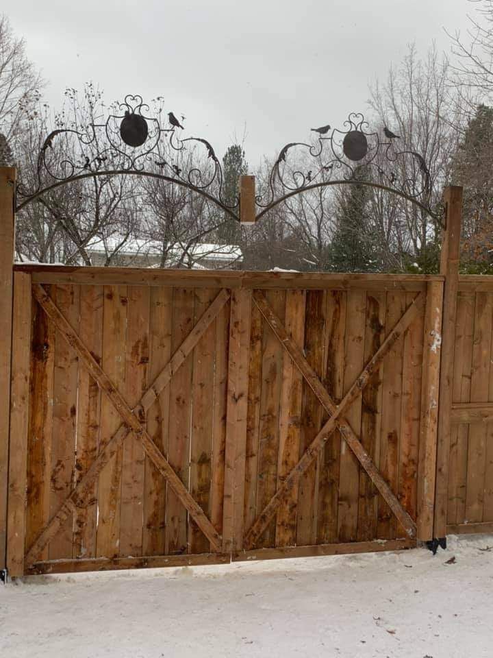 Portail en bois orné de ferronneries représentant des oiseaux et des cercles. Le sol est recouvert de neige.