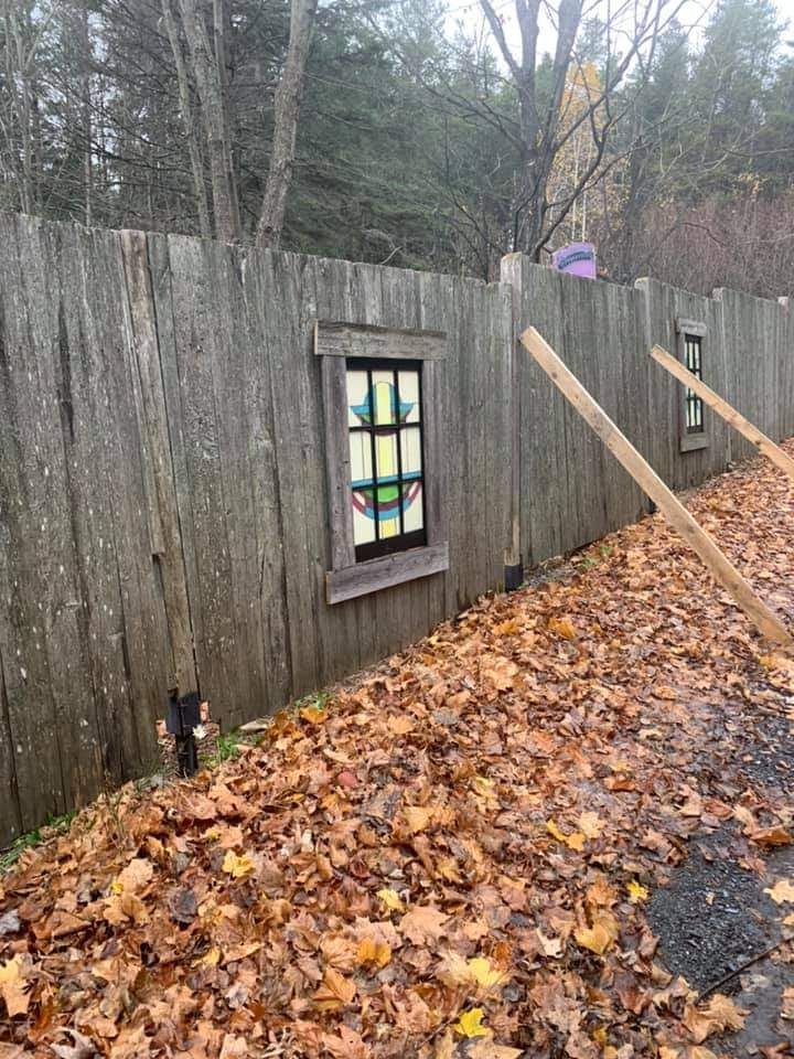 Clôture en bois avec vitrail décoratif, feuilles mortes au sol.