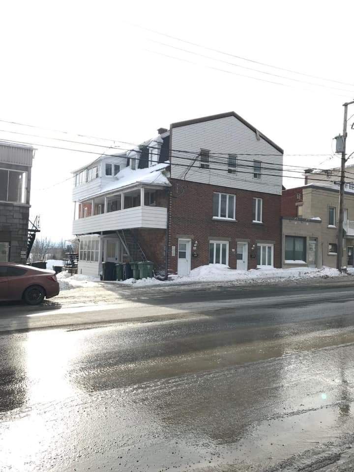 Immeuble en briques à plusieurs étages avec un balcon, neige au sol et rue devant.