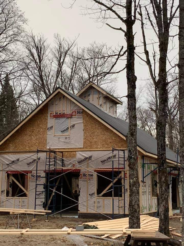 Construction d'un bâtiment avec charpente apparente, échafaudages et toit sombre dans une zone boisée.