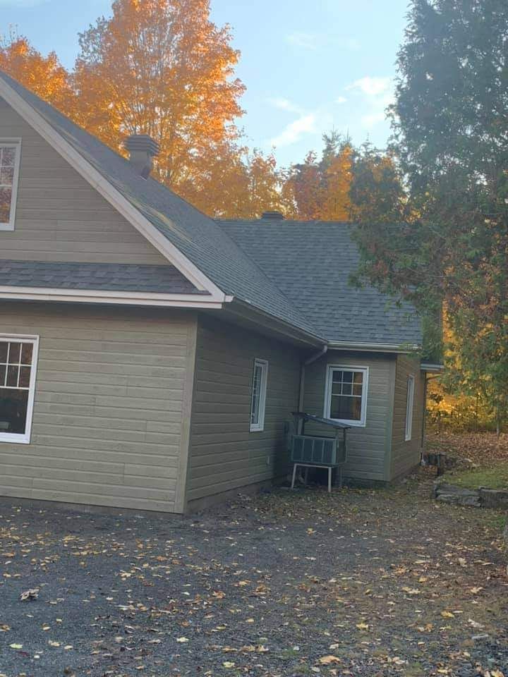 Maison beige avec toit gris, fenêtres grises et arbres d'automne.