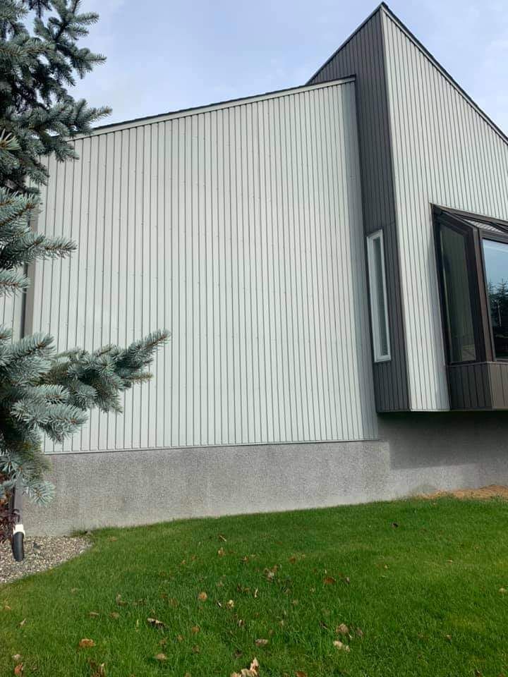 Maison moderne avec bardage vertical clair, touches de gris et une petite fenêtre.