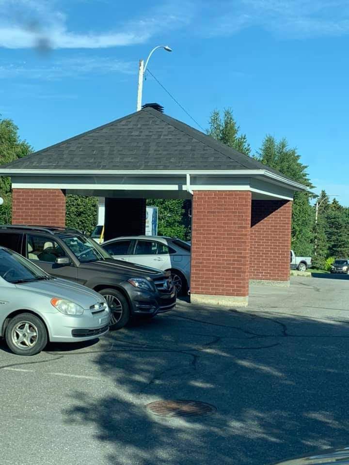 Des voitures garées sous un abri en briques et au toit par une journée ensoleillée.