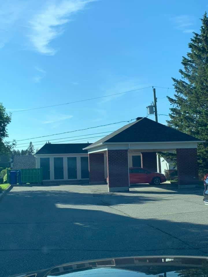 Un bâtiment en briques rouges avec une entrée couverte ; une voiture rouge est garée à l'intérieur. Ciel bleu.
