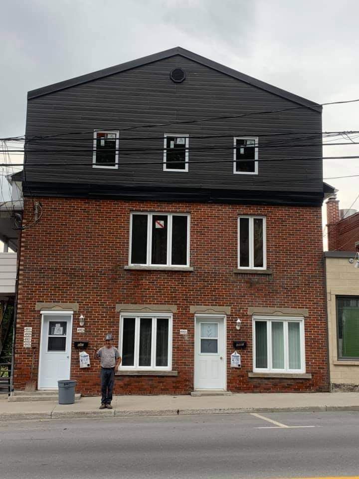 Bâtiment en briques avec un étage supérieur noir. Une personne se tient devant.
