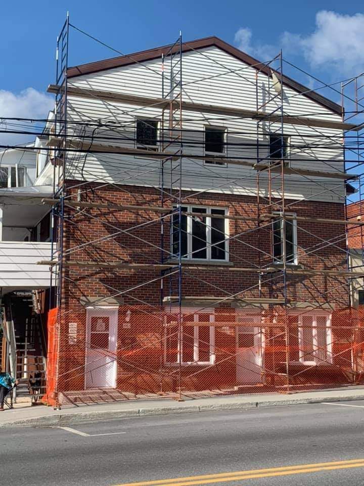 Bâtiment en construction avec échafaudages. Bardage blanc en partie supérieure, façade en briques en partie inférieure. Clôture de sécurité orange.